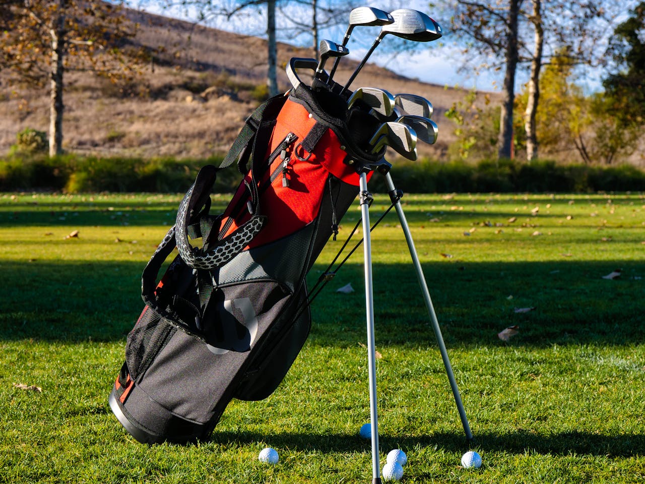 about-01 Red and black golf bag with clubs on a sunny golf course lawn outdoors.